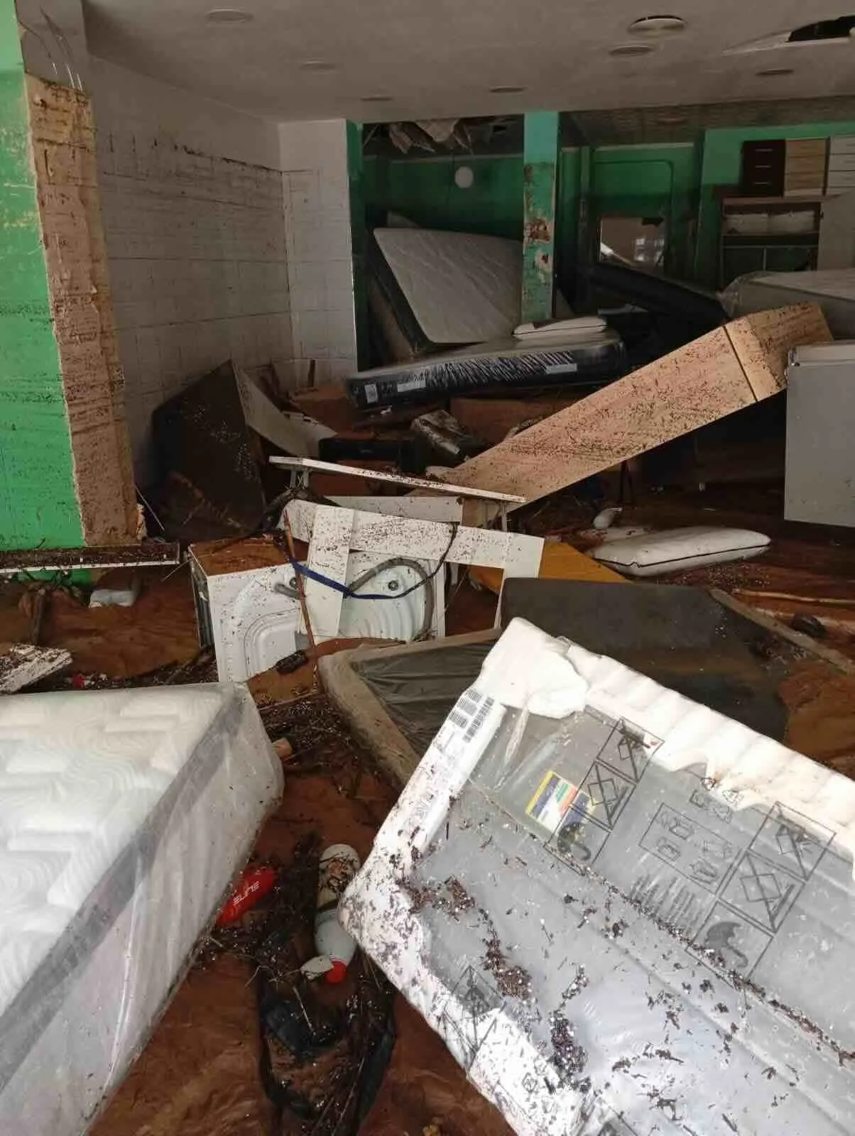 Interior de vivienda o local gravemente dañado por inundación, con mobiliario destrozado y barro acumulado tras el siniestro.